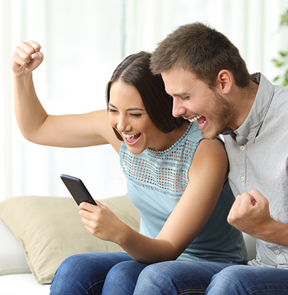 A photo of a couple sitting on a couch celebrating an auction win on their mobile device